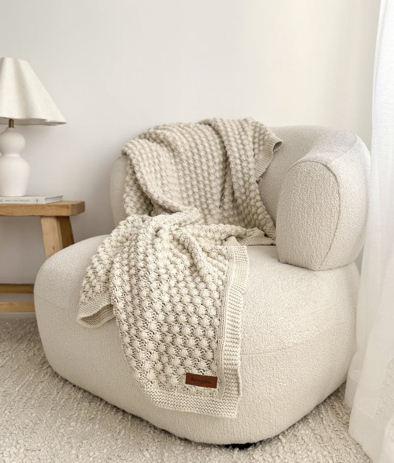 Bone Popcorn lounge throw in 100% cotton draped across a curved boucle armchair in a light, neutral room