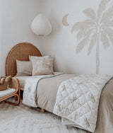 Bedroom with a rattan headboard, palm wall decal and a quilted palm throw over the dune sheet