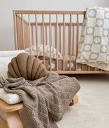Stone shell stitch blanket draped over a timber bench beside a cot with a shell cushion
