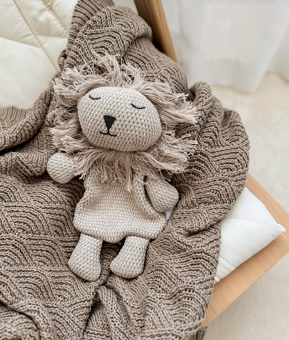 Greige knitted lion comforter lying on the stone shell stitch blanket