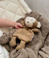 Knitted monkey comforter resting on the stone shell stitch blanket in a bassinet