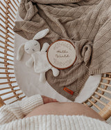 Overhead view of the stone blanket in a bassinet with a white bunny comforter and a Hello World disc