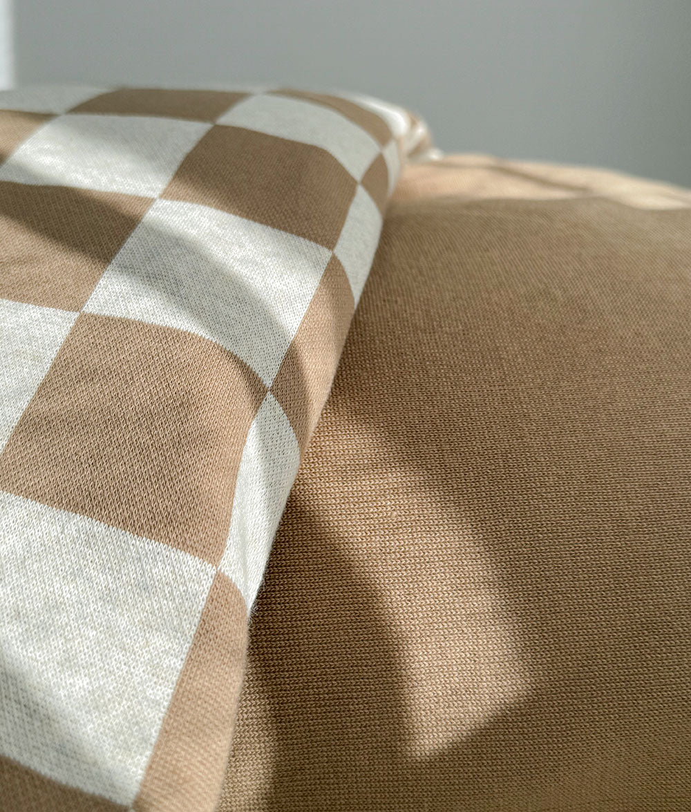 Close-up of a gingham check pillowcase resting against the plain khaki duvet cover