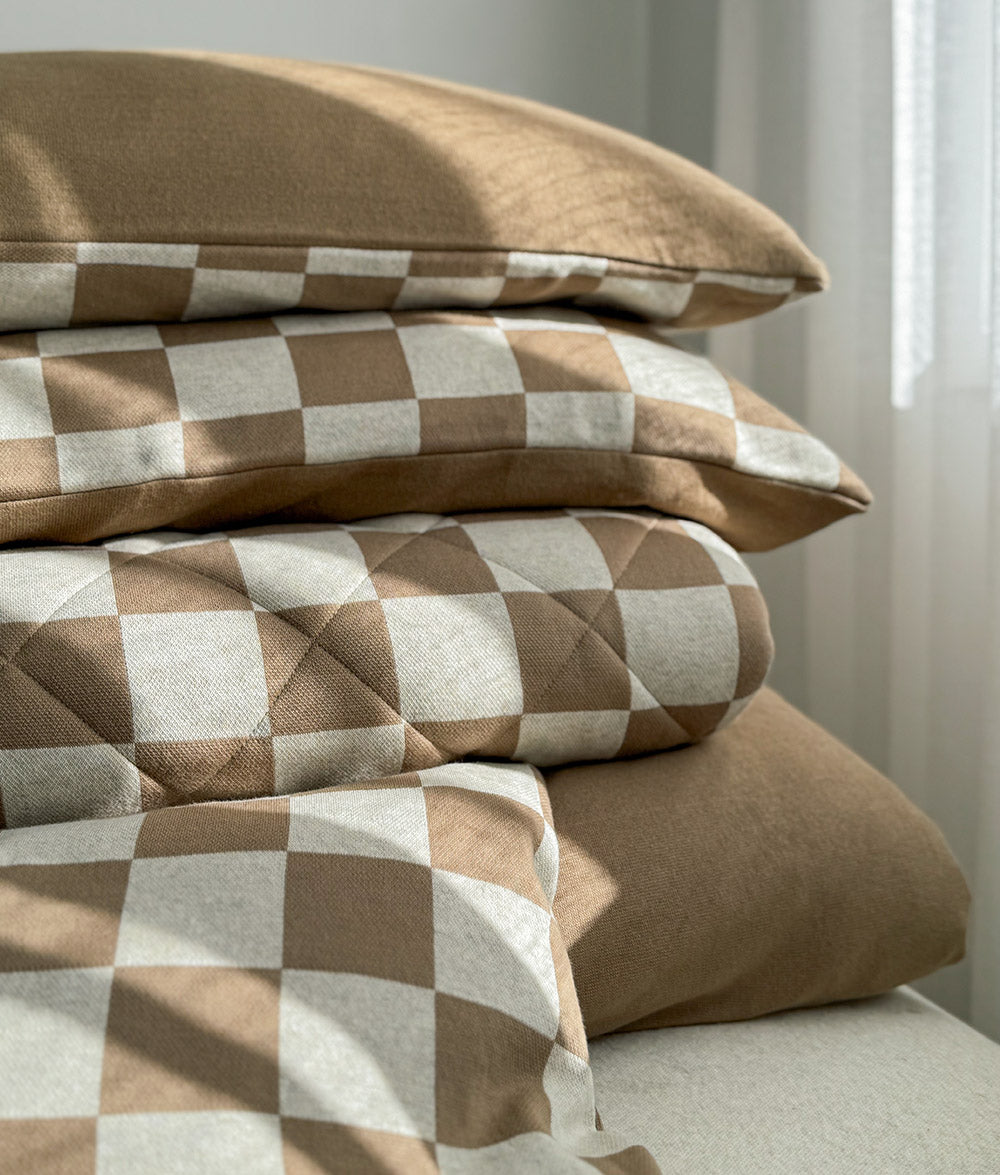 Folded stack of khaki gingham bedding with the check pillowcase on top