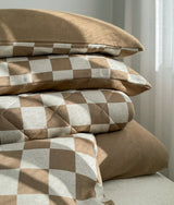 Folded stack of khaki gingham bedding with the plain khaki duvet cover underneath