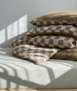 Stack of khaki gingham bedding folded on a bed in morning sunlight
