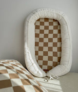 Baby lounger nest upright showing the khaki gingham check base and ivory cushioned surround