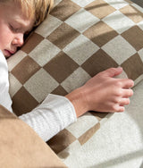 Child resting a hand on khaki gingham check bedding with the euro pillowcase beneath