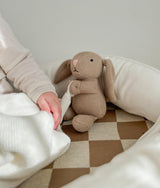 Child reaching towards a knitted bunny toy sitting in the khaki gingham lounger