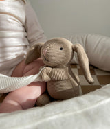 Knitted bunny toy propped in the khaki gingham baby lounger beside a baby