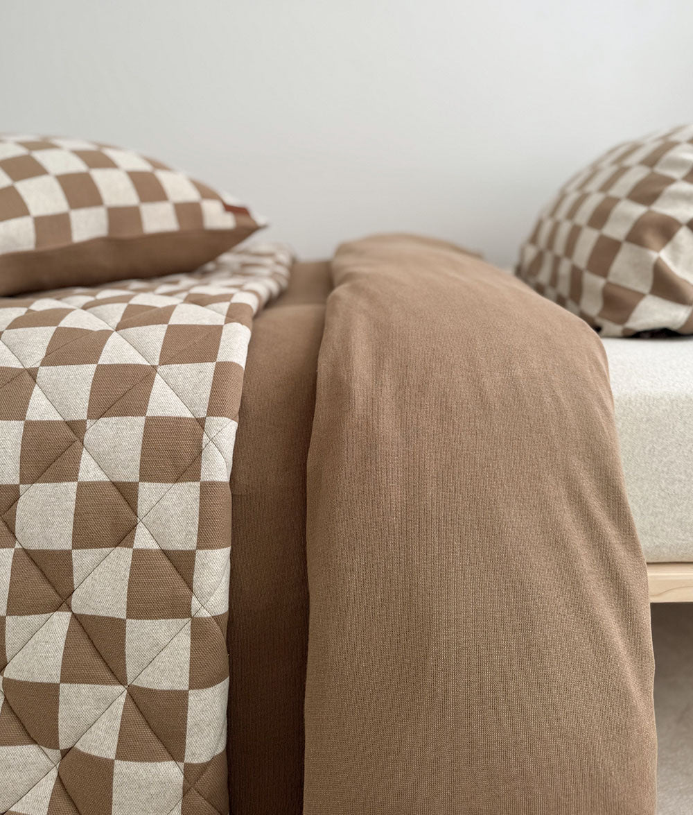Two beds side by side dressed in khaki gingham quilts and check pillowcases