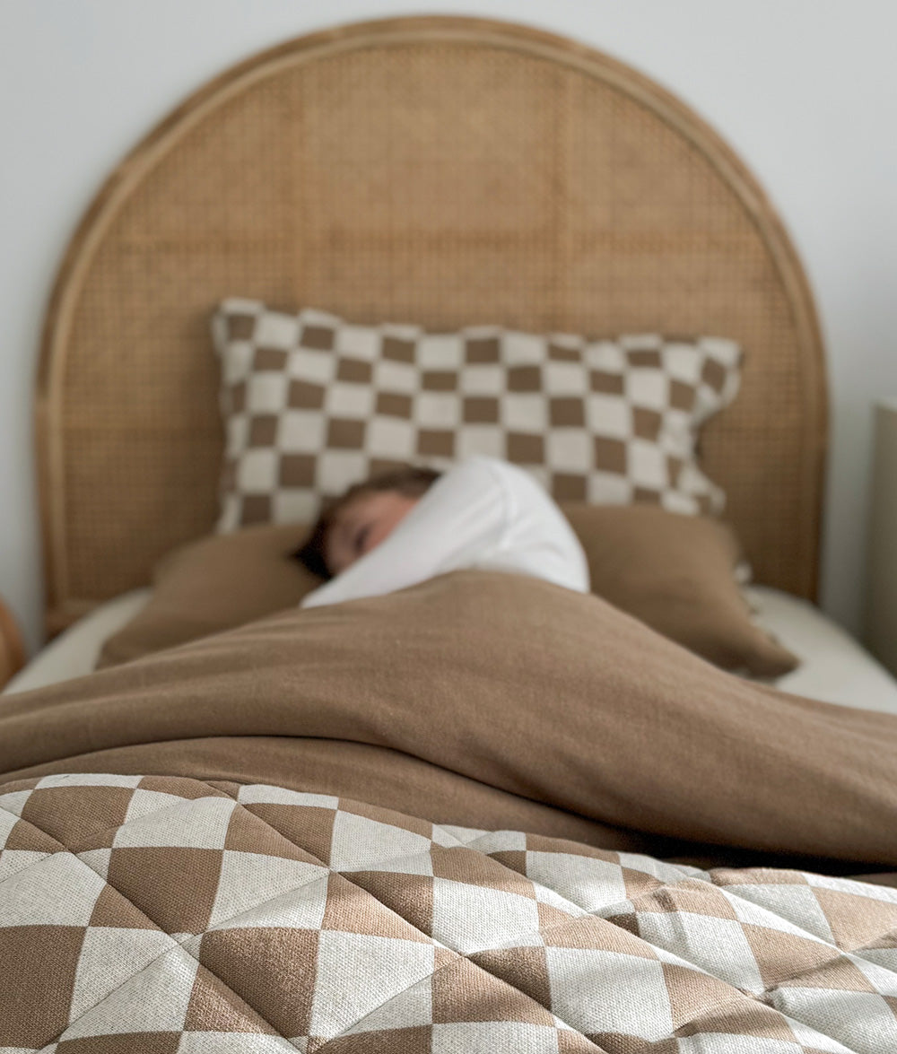Child asleep on a rattan bed with a khaki duvet and the gingham quilt across the foot
