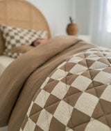 Close-up of the khaki duvet cover beside the gingham quilted layer on a bed