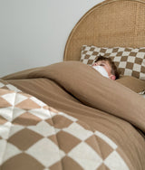 Child under a khaki duvet with the gingham check pillowcase behind them
