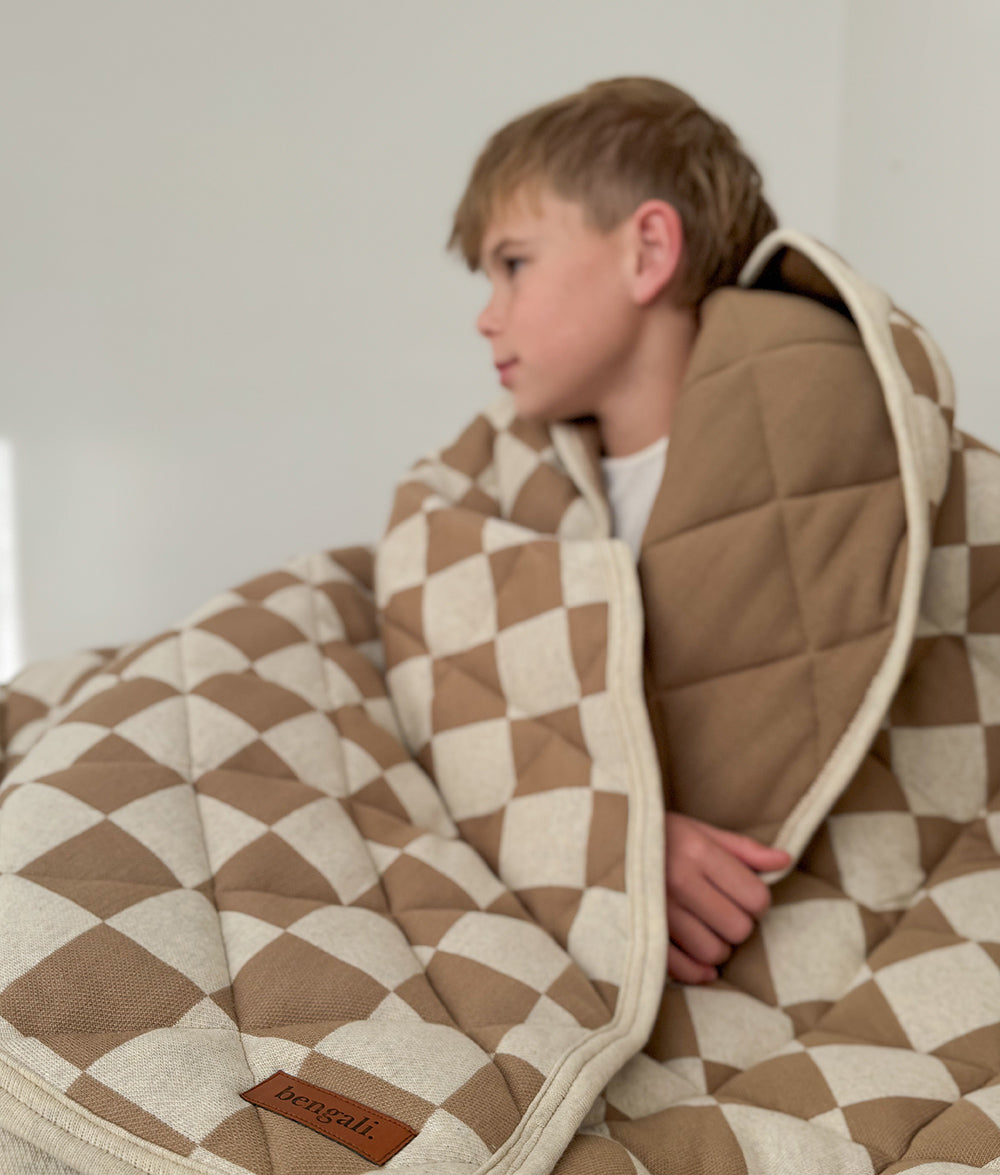 Child wrapped in the khaki gingham quilt showing the plain khaki brown reverse