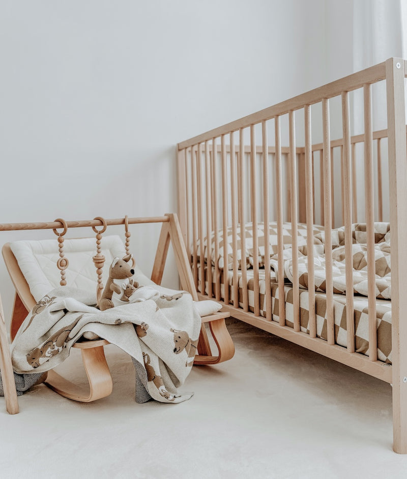Nursery with a timber cot and baby bouncer, the Kangaroo knitted baby blanket draped over the bouncer