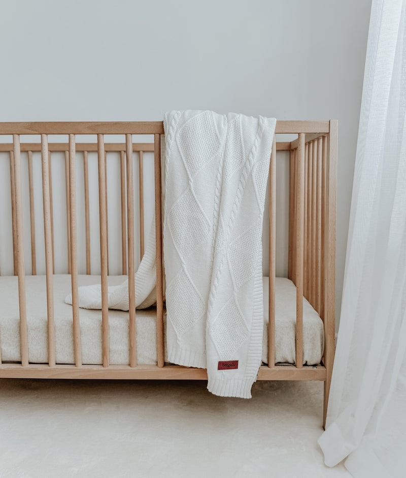 Ivory Diamante knit cotton lounge throw hung over the rail of a timber cot beside sheer curtains