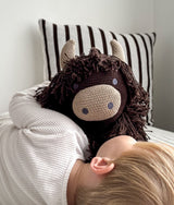 Close-up of a child cuddling Fergus the Highland cow against a chocolate striped pillow