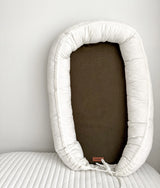 Baby lounger nest standing upright showing the olive base inside an ivory cushioned surround