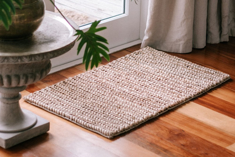 A Garcia Home Jute Mat Thick Tail Brown 60x90, hand-woven with jute fibers, placed in front of a potted plant.