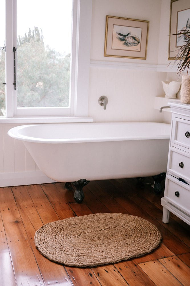 A white bathtub in a bathroom with natural, hand-woven Jute Mat Braided Oval Brown 60x90 fibres on the wooden floors by Garcia Home.