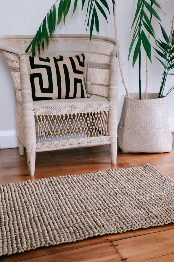 A Jute Rug Bubble Natural Brown made by Garcia Home, hand woven with jute fibers, was laid on a wooden floor next to a chair and a potted plant.