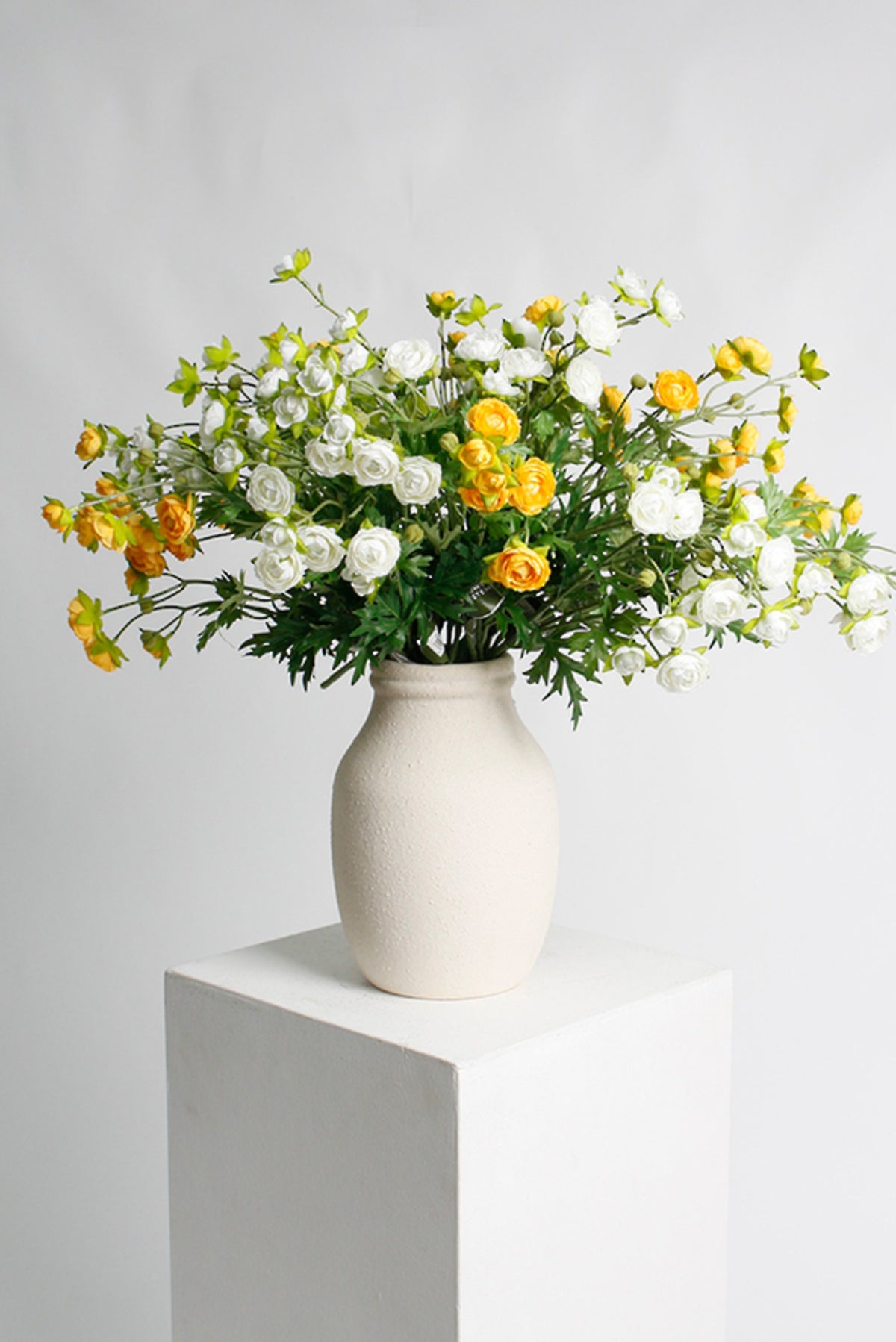 White petite ranunculus sprays styled with yellow ranunculus in a white vase