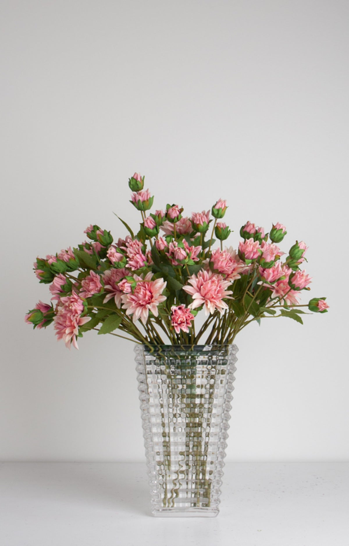 Bunch of aged pink mum sprays in a tall clear cut glass vase