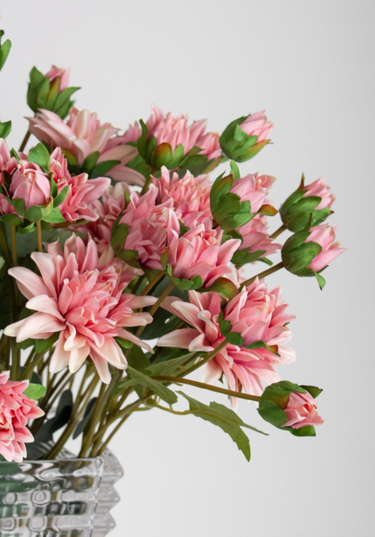 Close view of aged pink chrysanthemum blooms above a cut glass vase