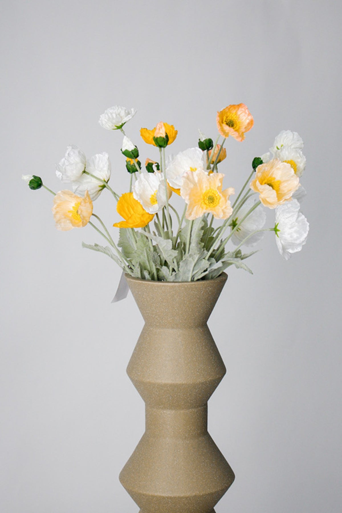 White, blush and apricot poppies in a tall stacked beige ceramic vase