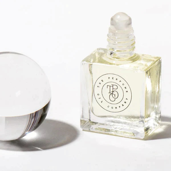 Roll-on perfume oil bottle with the cap removed, beside a glass sphere