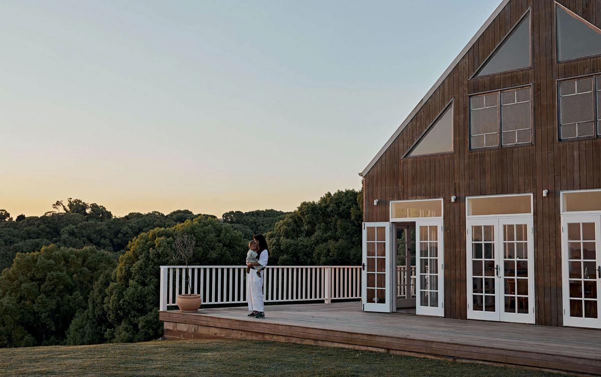 A woman standing on the deck of a house in Byron Bay, showcasing the Home By The Sea Books.
