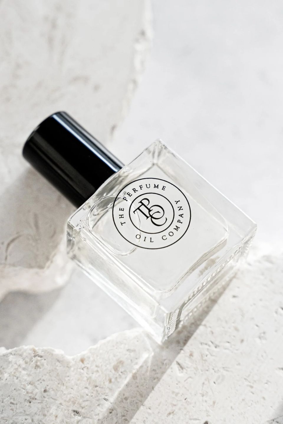 Clear cube roll-on perfume oil bottle with a black cap resting on textured white plaster