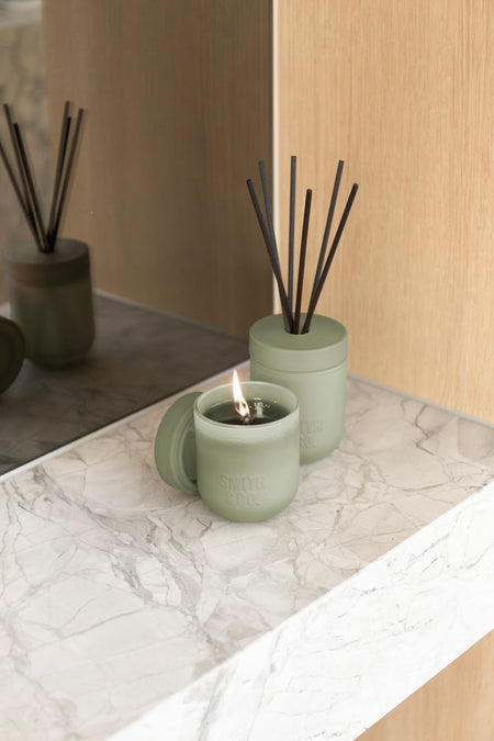 Lit Smith and Co candle and a reed diffuser on a marble ledge by a timber panel