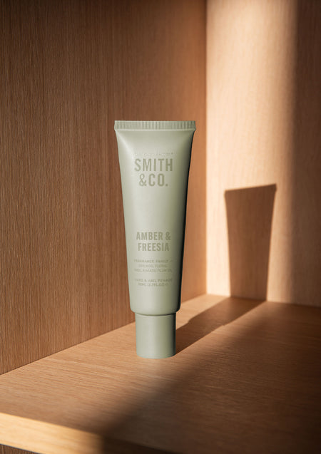Sage green Smith & Co. hand cream tube standing on an oak shelf in warm sunlight