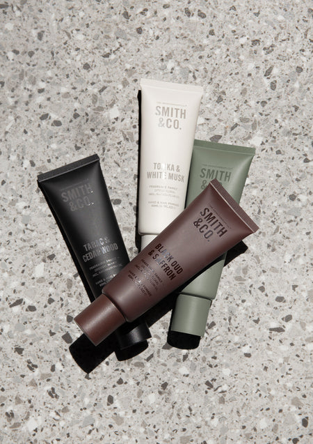 Four Smith & Co. hand cream tubes in black, white, brown and sage fanned out on grey terrazzo