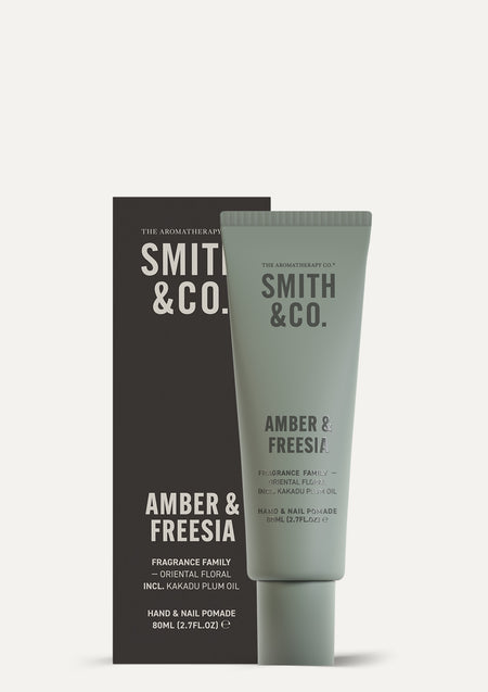 Smith & Co. Amber & Freesia pomade tube in front of its charcoal box on a pale background