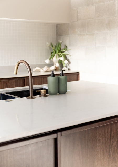 Kitchen sink with a brass tap and Smith & Co. bottles on a white benchtop