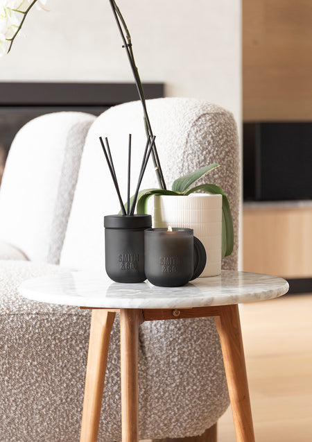 Smith & Co. diffuser and candle on a marble side table beside a boucle armchair