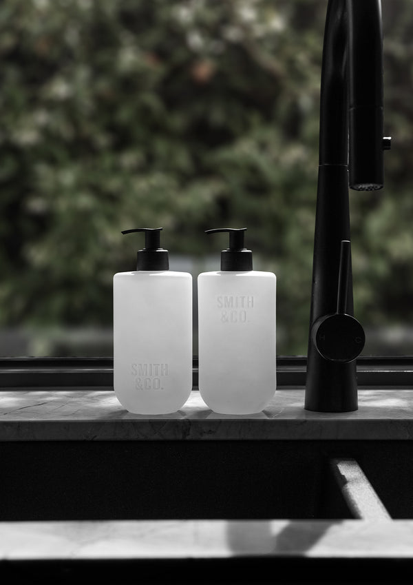 Two frosted Smith and Co bottles on a kitchen bench beside black tapware and a window