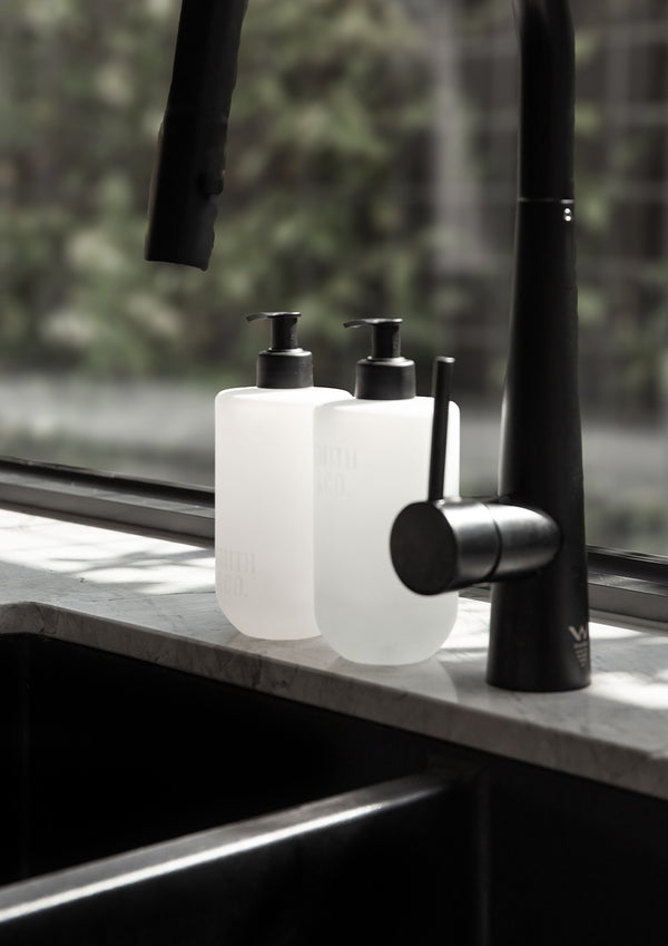 Two Smith and Co bottles beside a black kitchen tap with a garden view behind