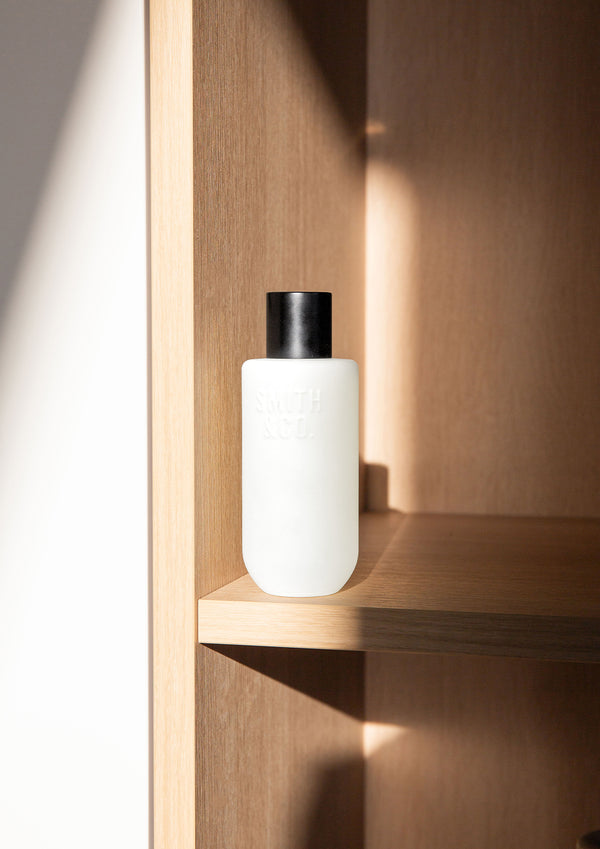 Frosted room spray bottle on a pale timber shelf set into a warm timber niche