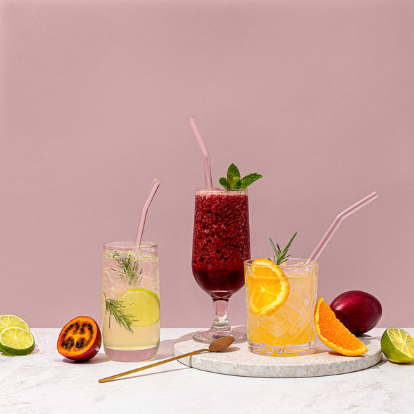 Four Sucker reusable glass drinking straws - transparent / multi-coloured on a marble tray.