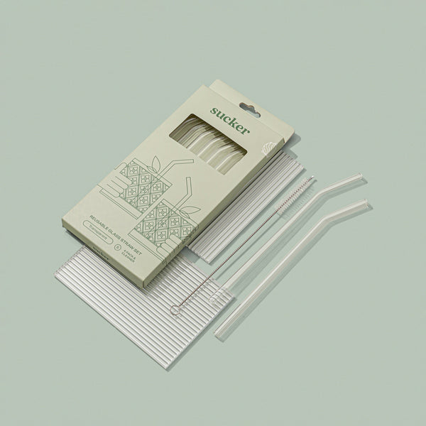 A set of Sucker reusable glass drinking straws in a package on a green background.