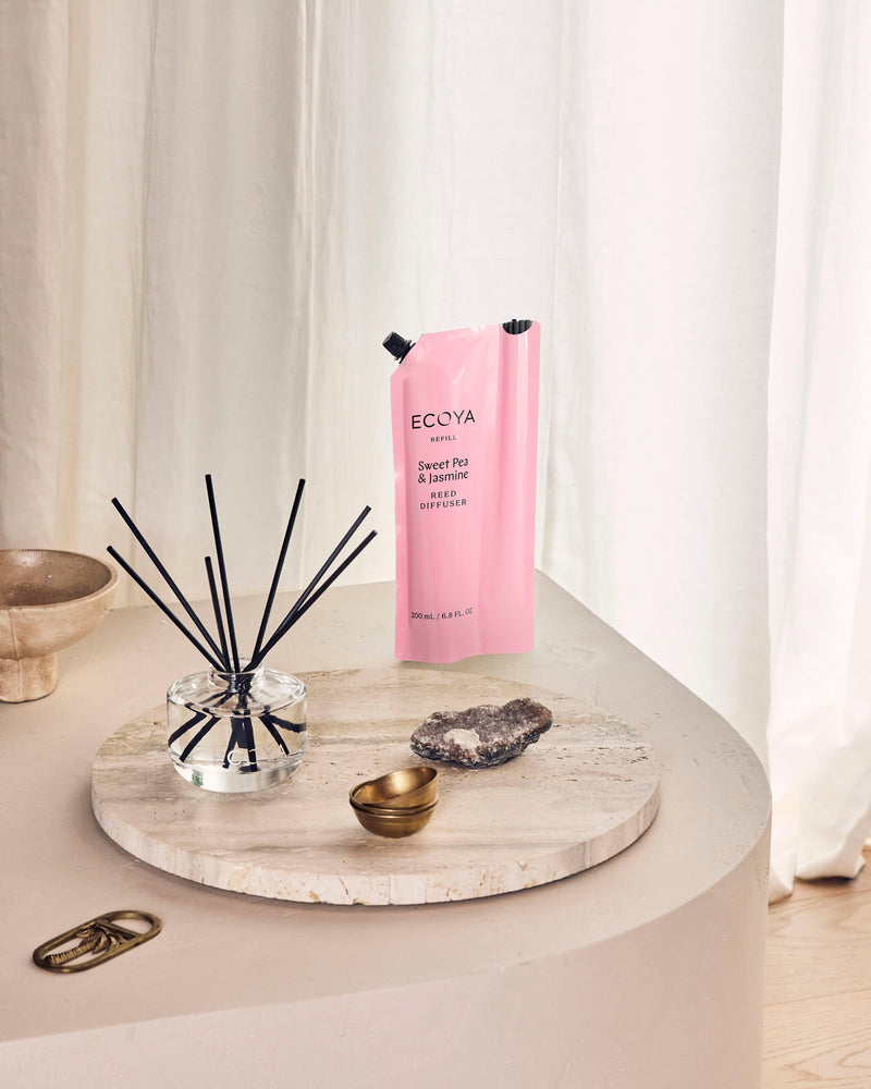 Ecoya Sweet Pea and Jasmine reed diffuser with its pink refill pouch on a travertine tray