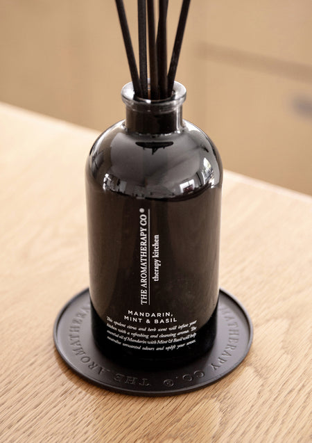 Black Therapy Kitchen reed diffuser standing on the round black plate on light oak