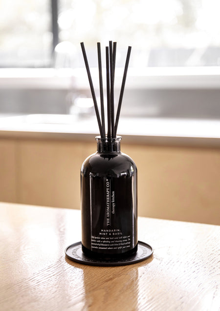 Black reed diffuser on the black plate on a timber table with a bright window behind