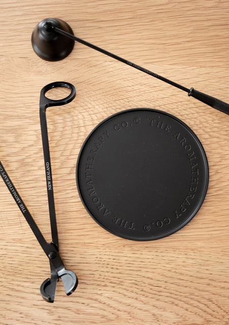 Round black embossed plate with a candle snuffer and wick trimmer on light oak, from above