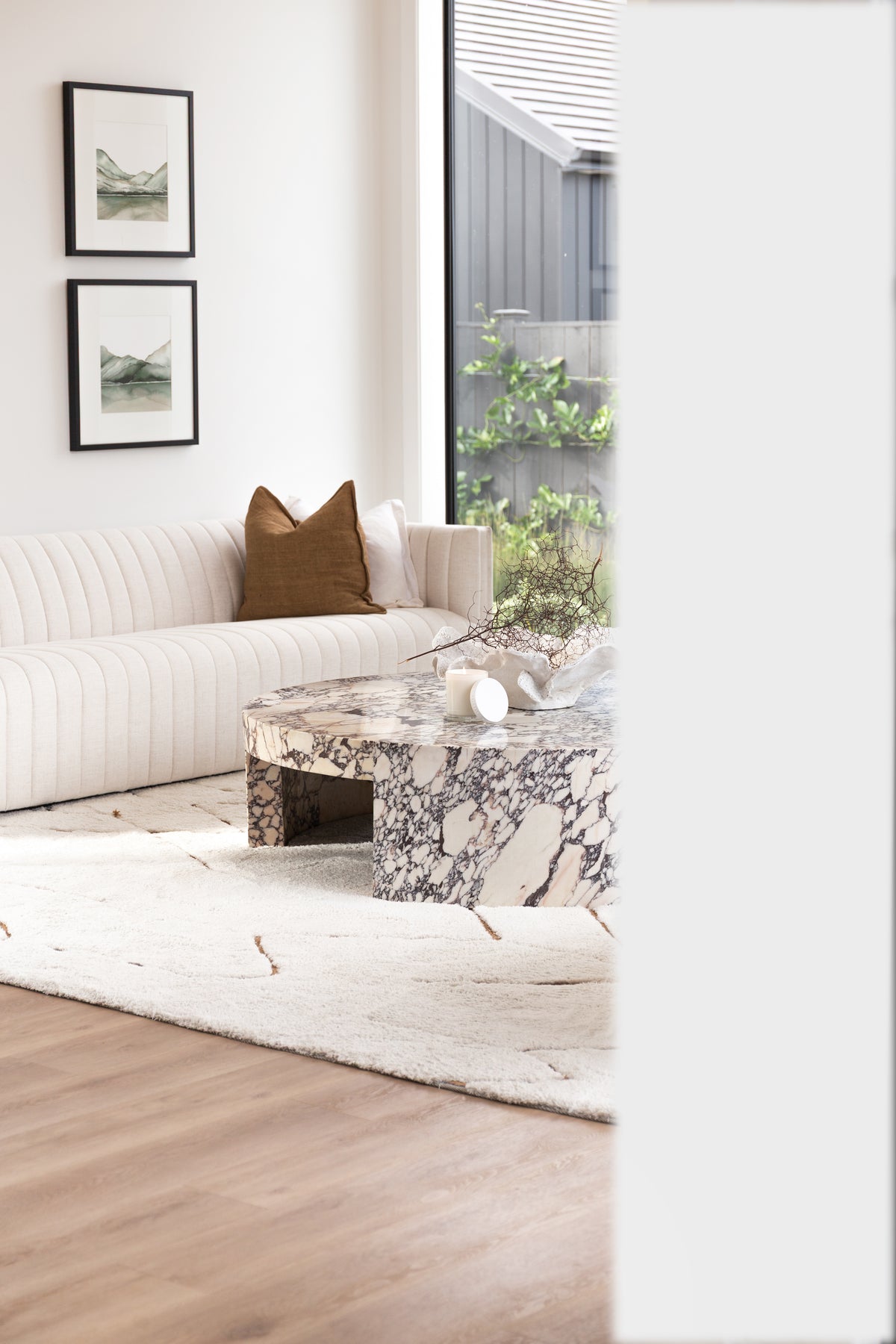 Living room with a fluted sofa, framed prints and a marble coffee table by the window
