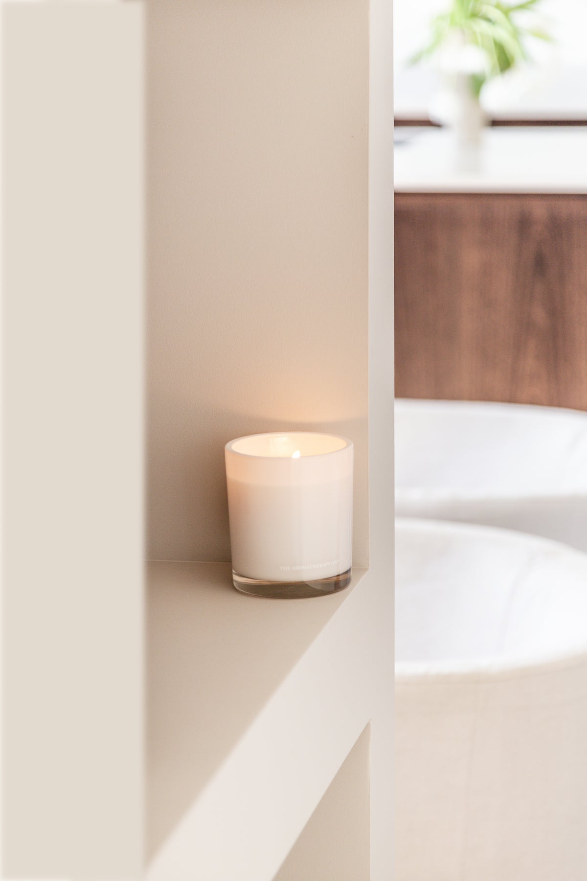 Naturals candle on a white ledge in a bathroom with the bath beyond